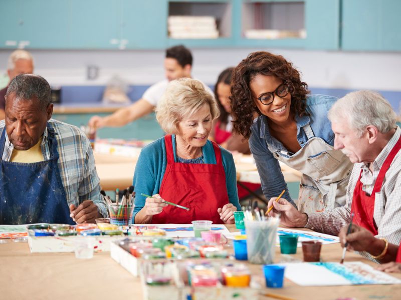 A group of seniors painting with assistance in a senior living community.