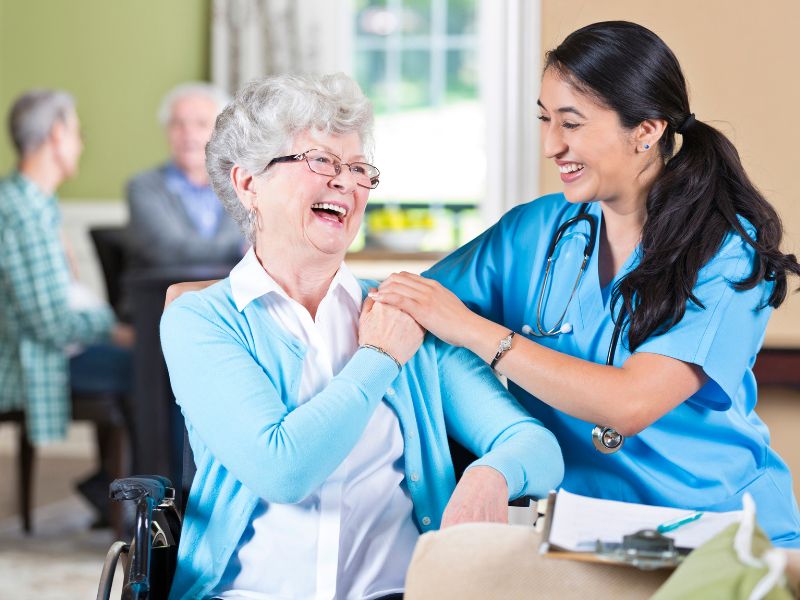 A senior and a nurse laugh and spend time together in an assisted living community room.